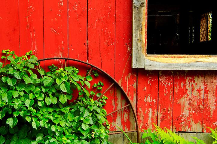 A close up of an antique wheel resting against a red building