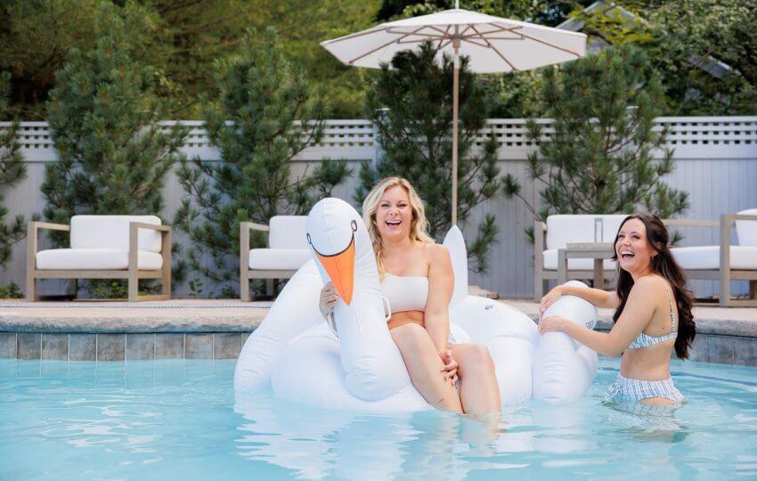 Two people on an inflatable swan in a pool
