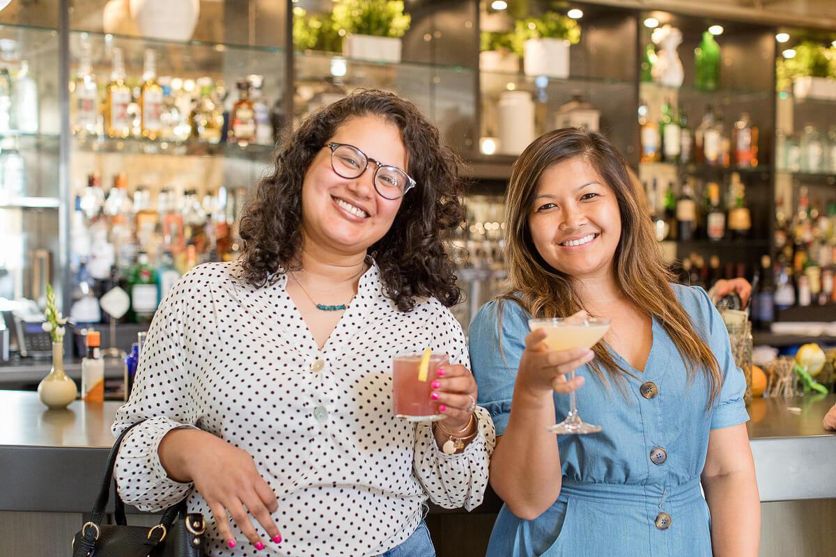 Two people smiling at the camera with drinks in hand