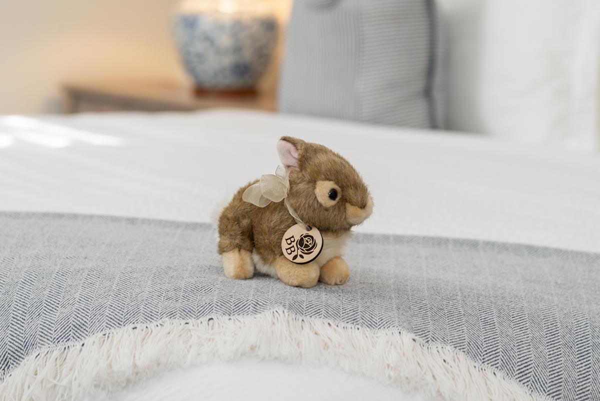 Plush rabbit with a heart tag on a bed.
