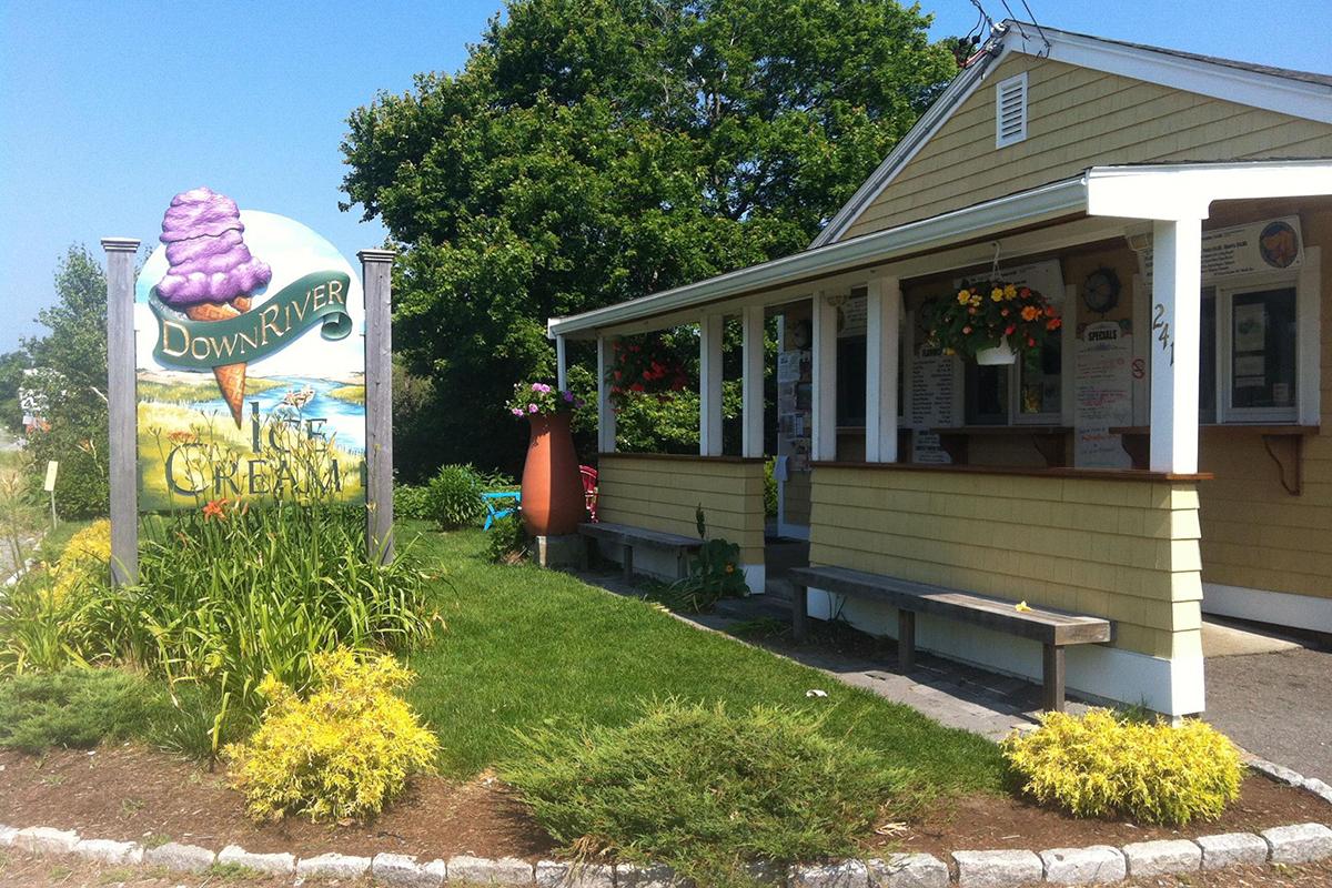 Ice cream shop with sign and garden in sunny setting.