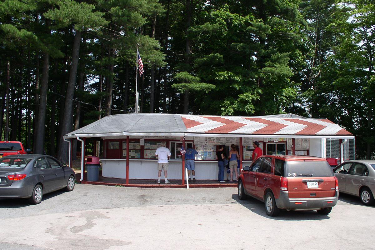 Small roadside diner with red cars parked, surrounded by trees.