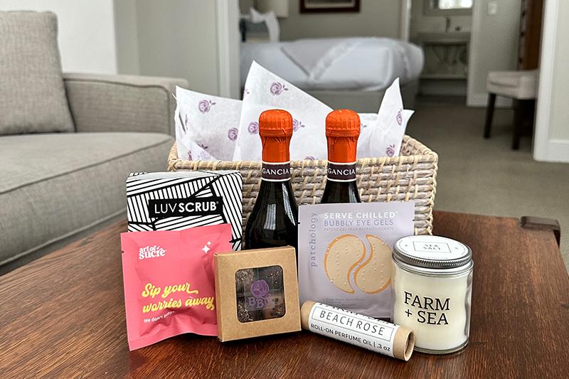 Gift basket with snacks, candles, and drinks on a wooden table in a cozy room.