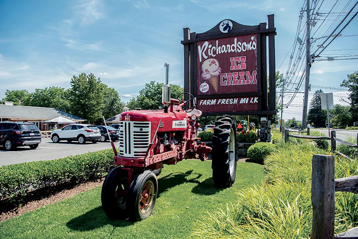 Red tractor next to an ice cream stand sign under a clear blue sky.