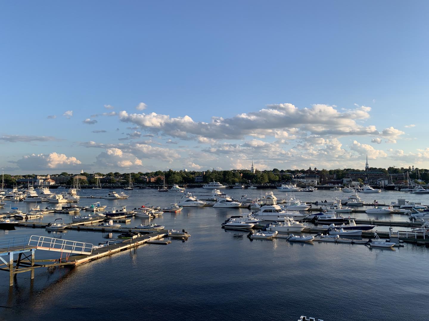 Boats docked in a calm marina under a clear blue sky with scattered clouds.