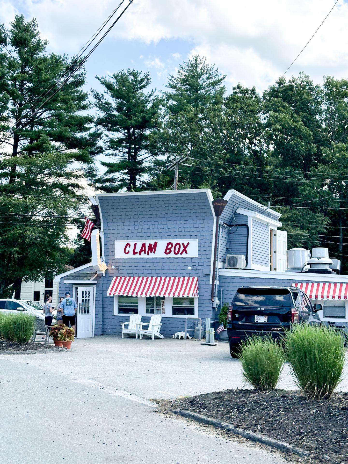 A small, gray diner with red and white striped awnings, surrounded by trees.