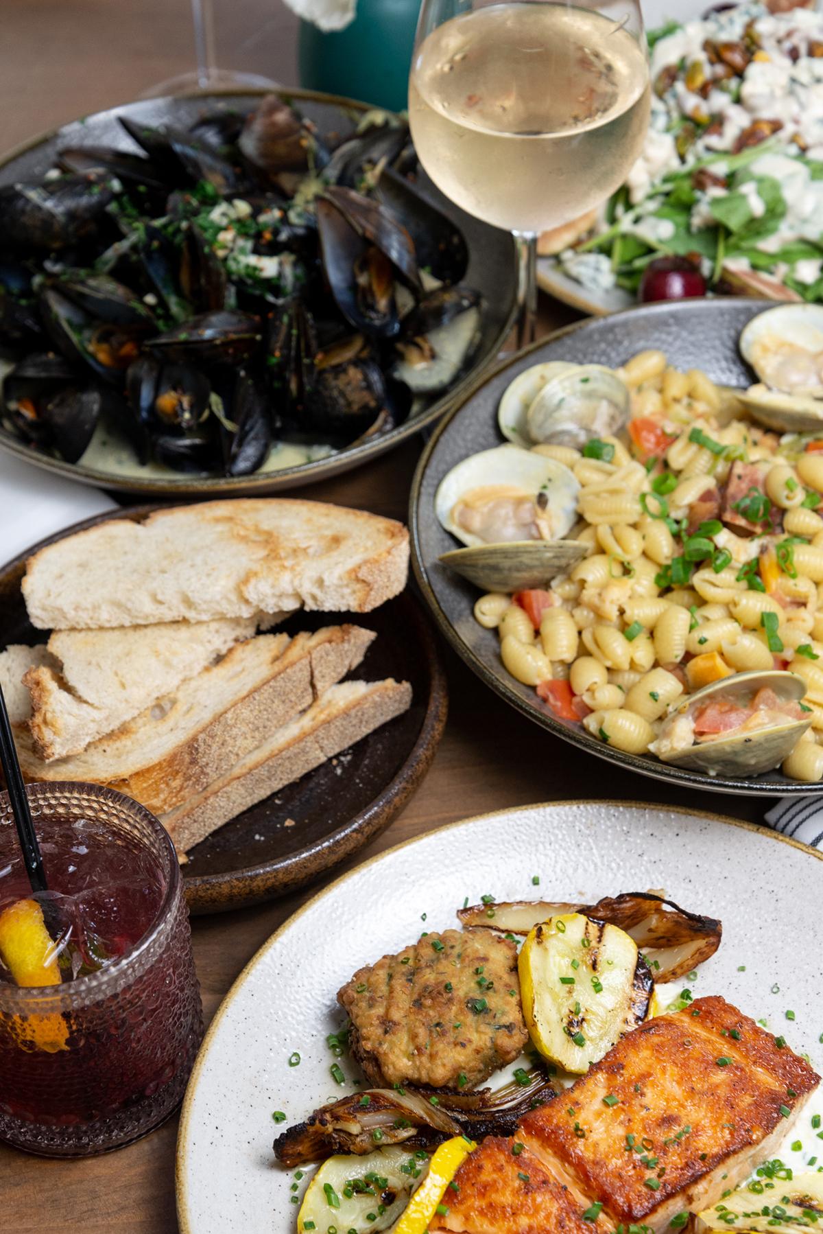 Seafood dishes with bread, salad, a cocktail, and a glass of white wine on a table.