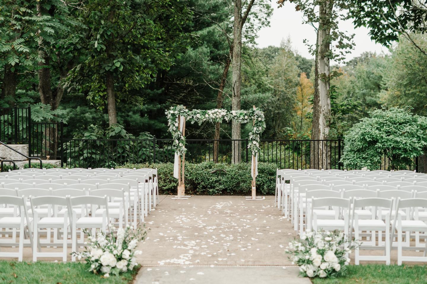 Outdoor wedding ceremony setup with white chairs and floral arch