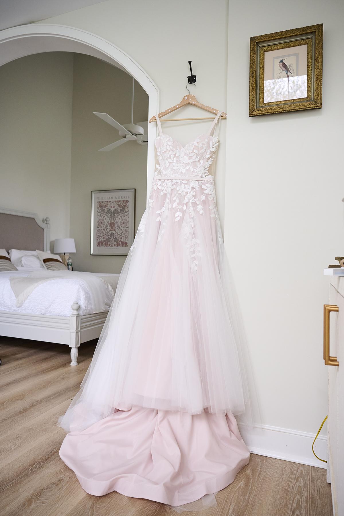Elegant white wedding dress hanging in a serene, cozy bedroom.