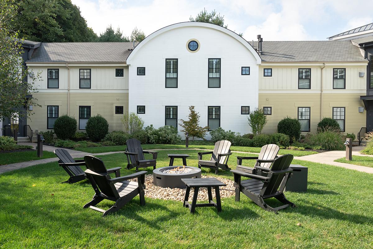 Chairs around fire pit in garden with a large house in background.