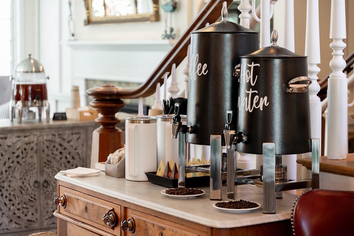 Coffee and tea urns on a wooden counter near stairs.