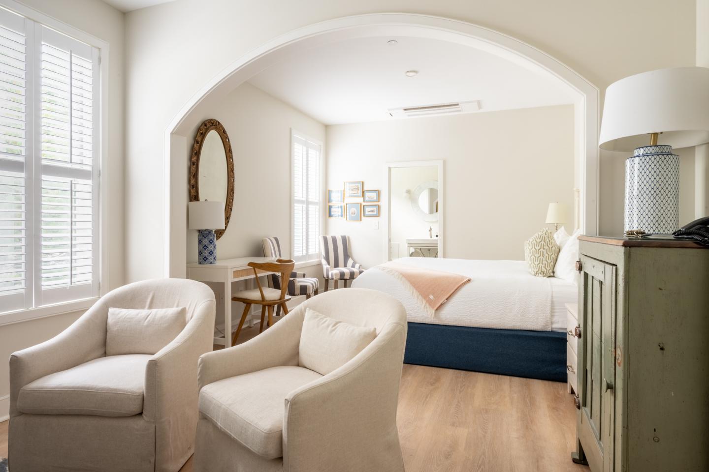 Cozy, light-filled bedroom with armchairs, bed, and desk under an arched entry.