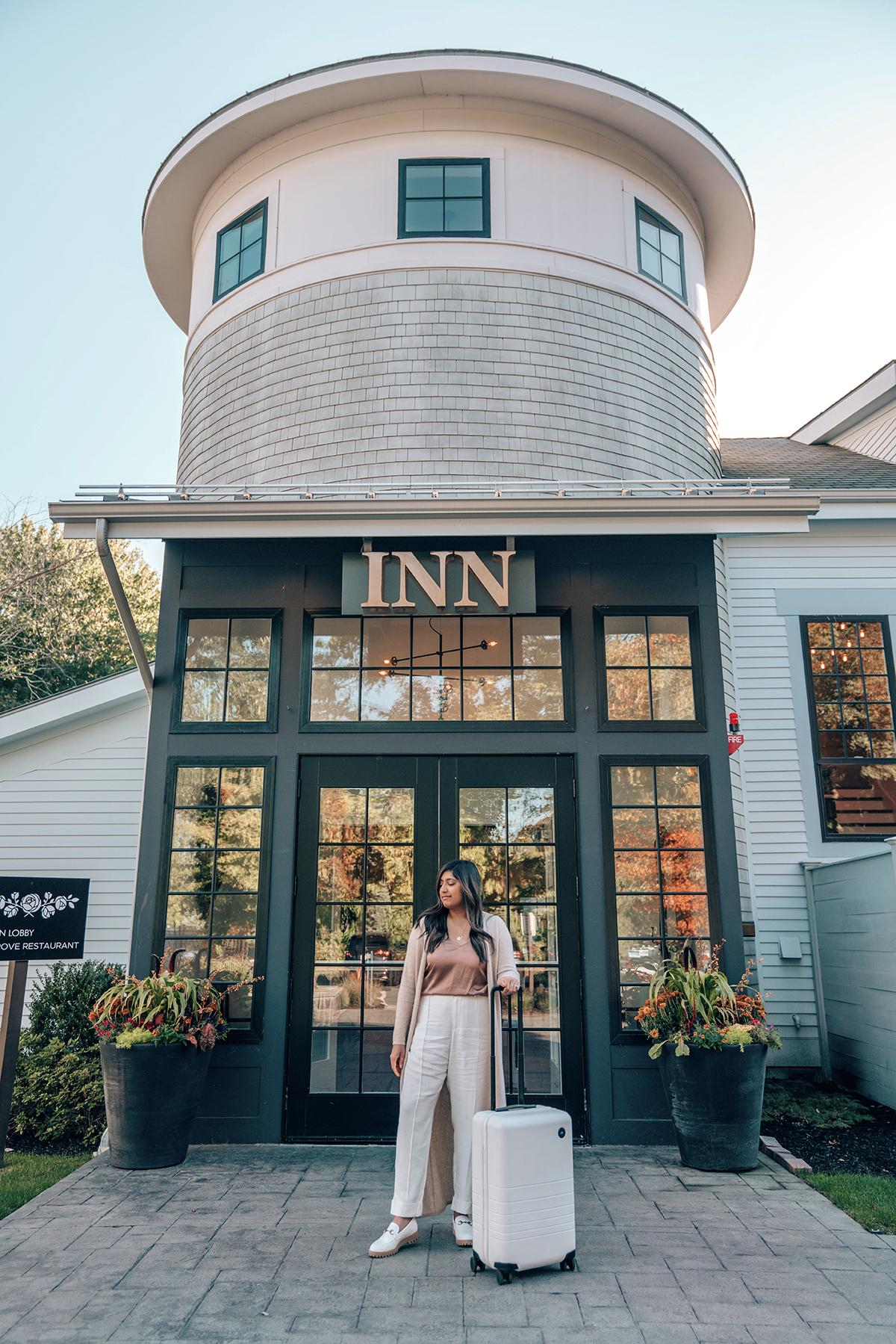 Woman with suitcase in front of a small inn, under a clear sky.