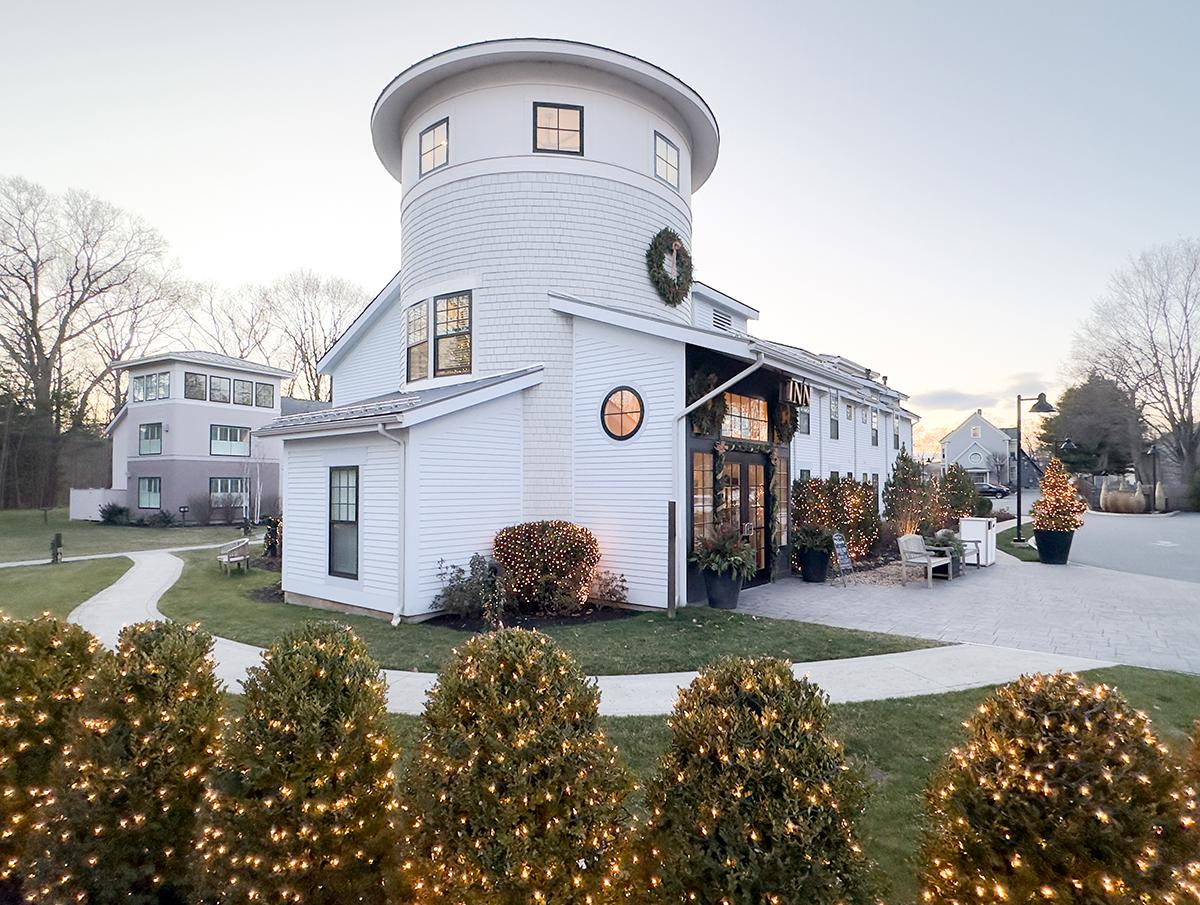 White house with turret, holiday lights, and wreaths during sunset.