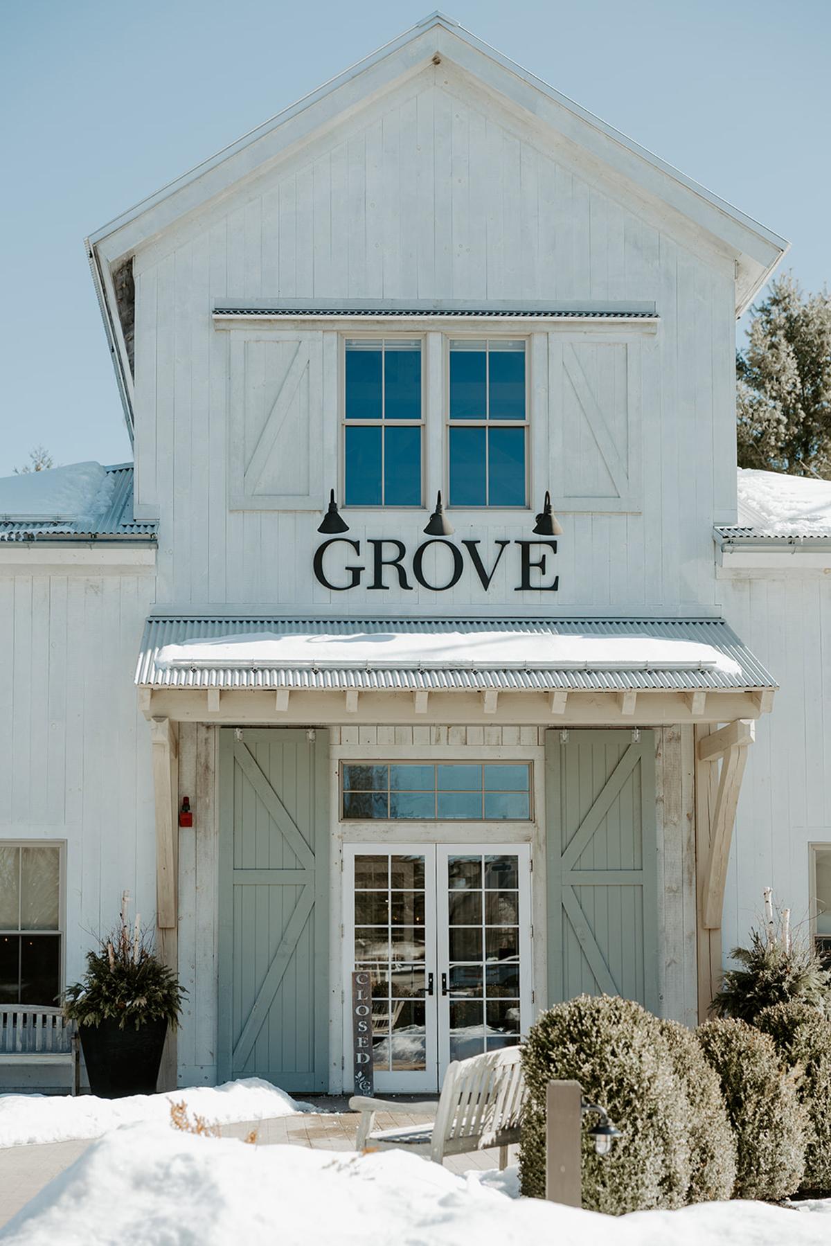 White building with "GROVE" sign, snow on ground, clear blue sky.