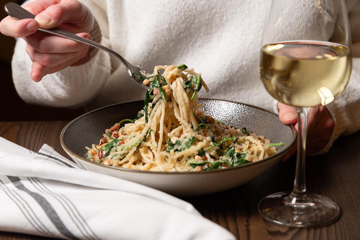 Spaghetti with herbs next to a glass of white wine on a table.