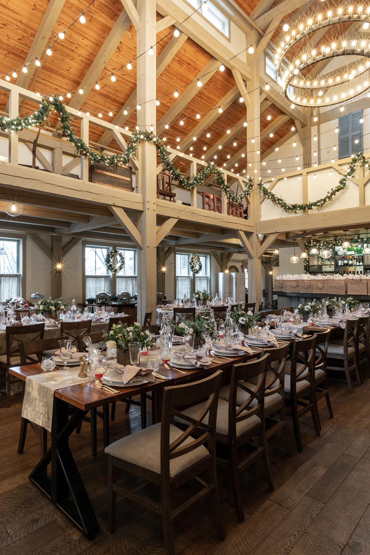 Rustic dining hall set for an event, with strings of lights and greenery.