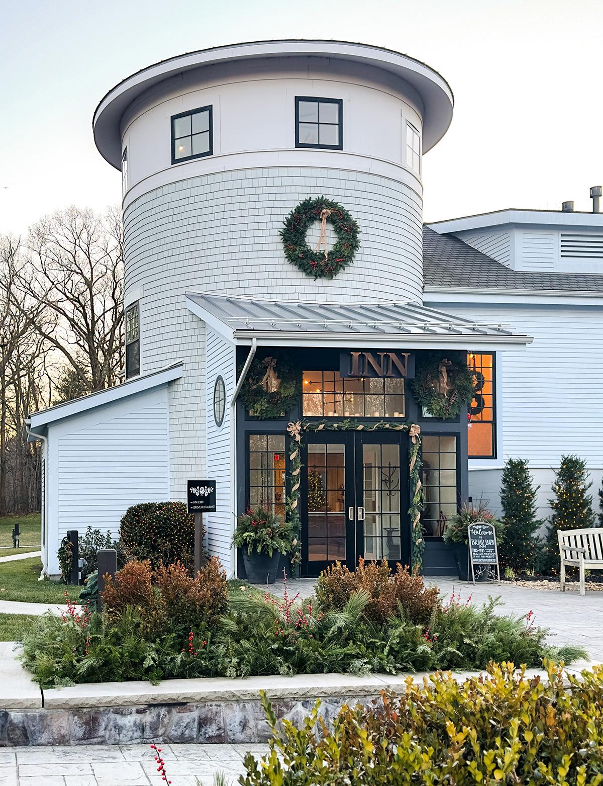 White building with tower, wreath on top; decorated inn entrance, greenery and path in front.