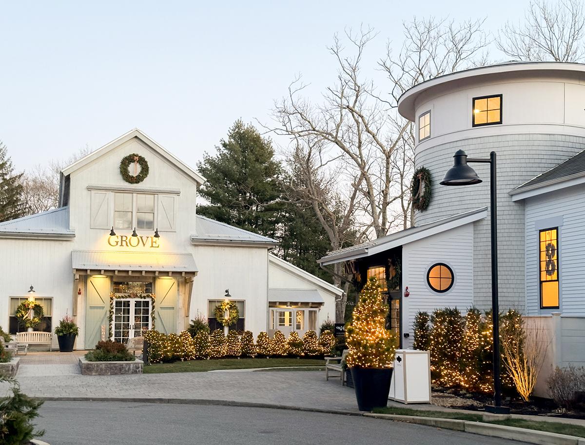 Festively lit buildings with wreaths and glowing trees at dusk.