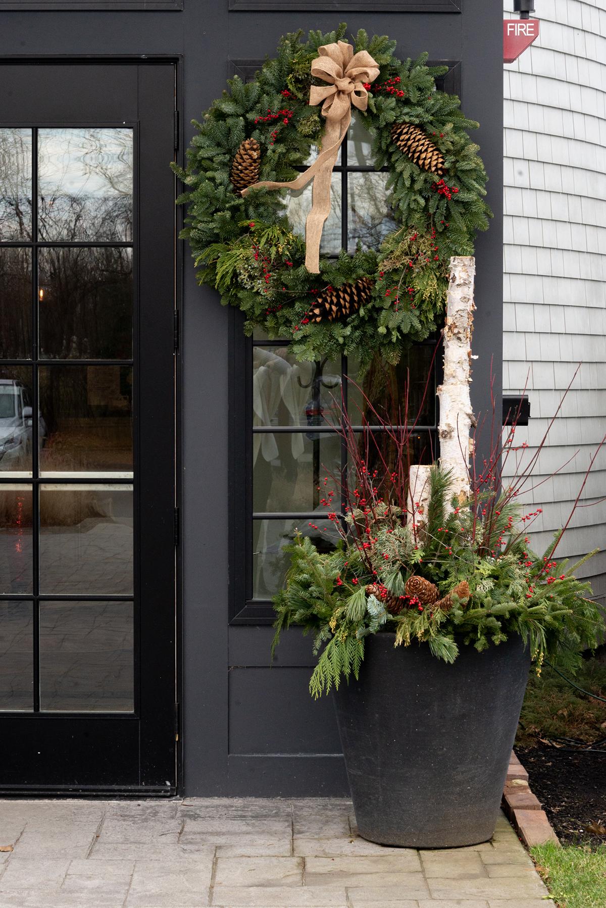 Christmas wreath and greenery pot by a black door.