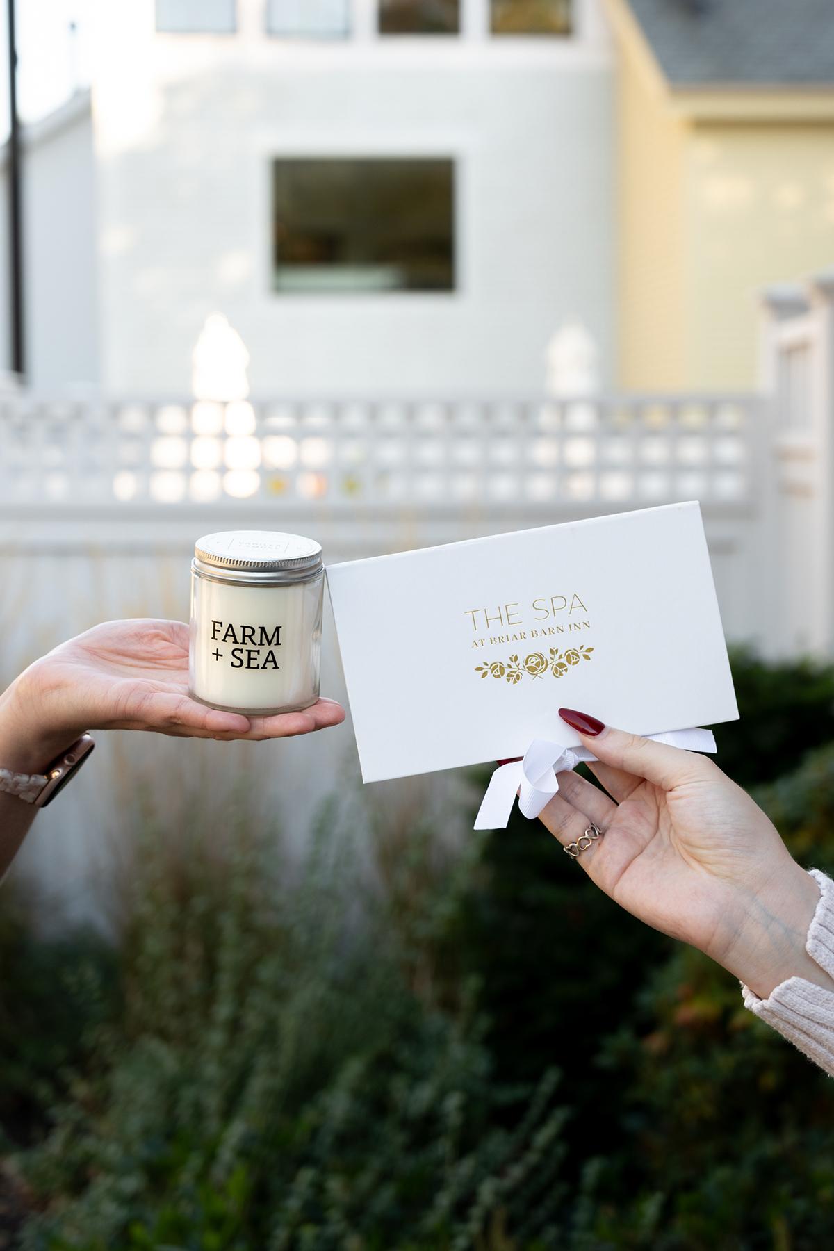 Two hands holding a candle and envelope outdoors near a white fence.