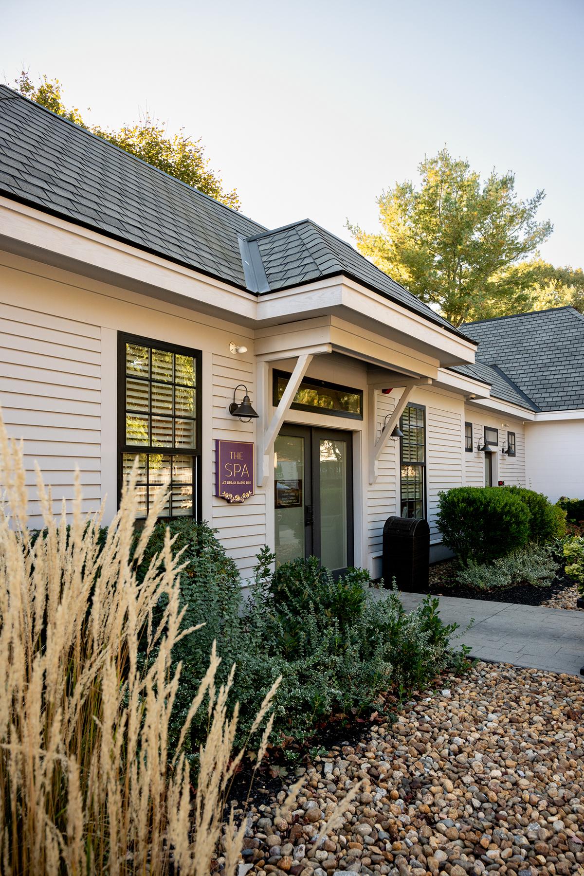 White building with gray roof, surrounded by plants and rocks, under a clear blue sky.