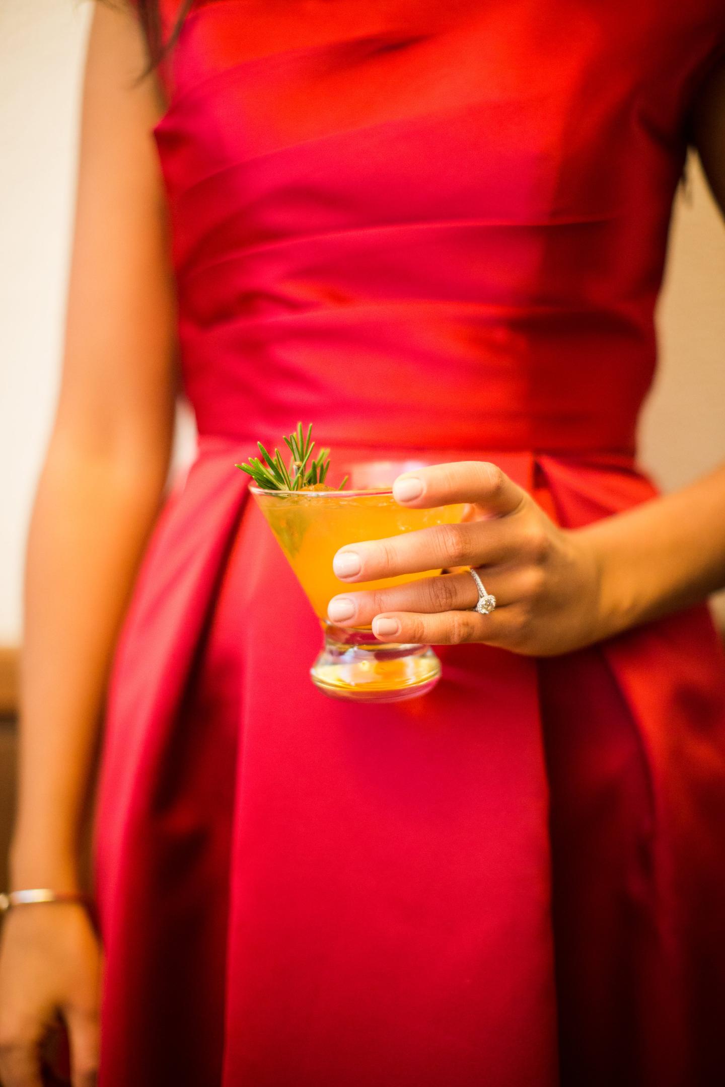 Woman in red dress holding a cocktail with herbs.