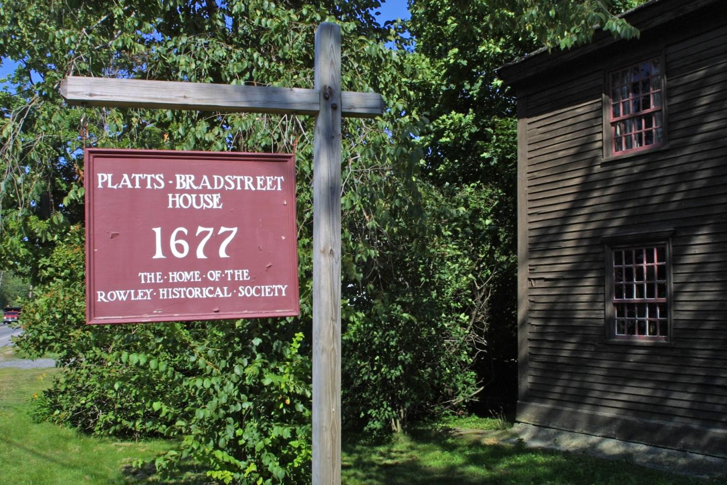 Sign reading "Platts Bradstreet House 1677" next to a historic wooden building.