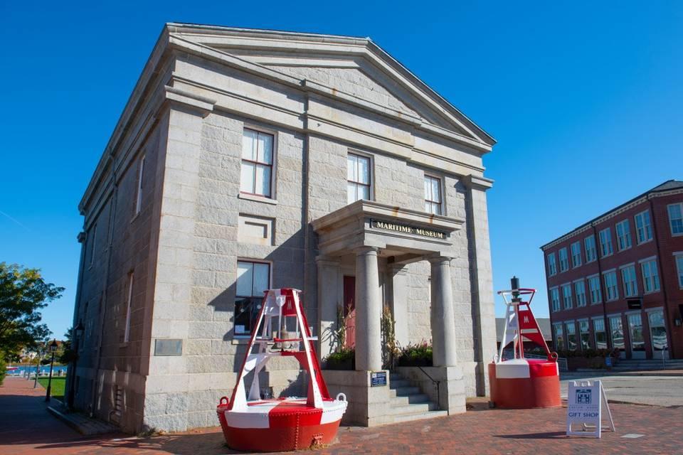 Historic stone building with columns, red structures in front, under a clear blue sky.