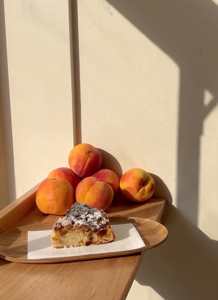 Peach pie slice on tray beside whole peaches in sunlight.
