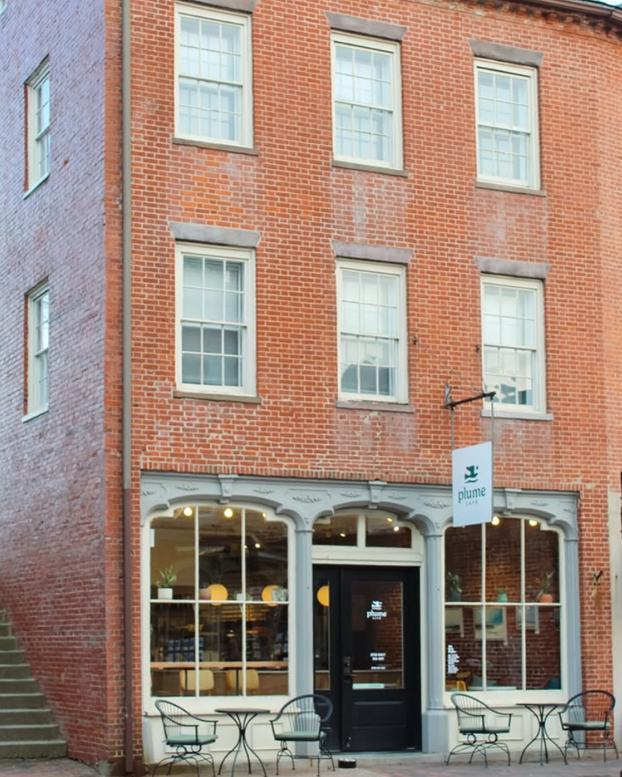 Red brick building with a black door, arched windows, and outdoor seating.