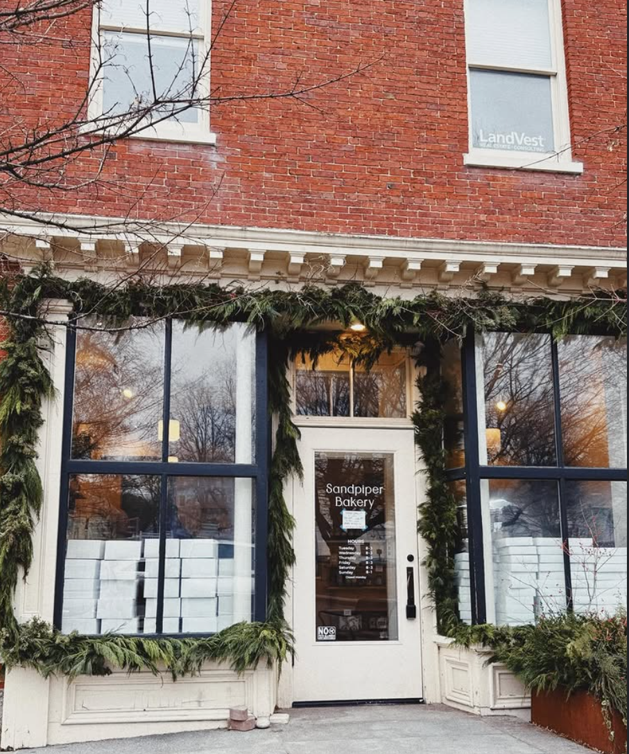 Brick building with large windows, door, and festive green garlands.