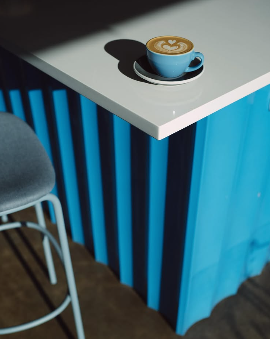 Coffee cup on a white table next to a blue chair and wall.