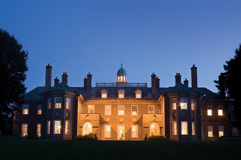 Illuminated mansion at dusk with a symmetrical facade and cupola.