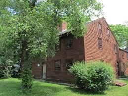 Rustic brown wooden house with large tree and green bushes.