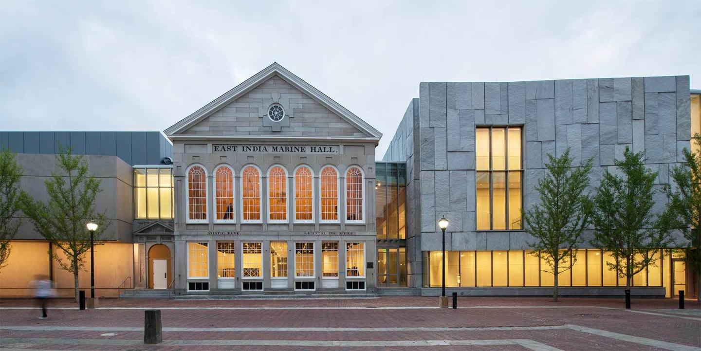 Historic and modern building facade with warm-lit windows and trees.