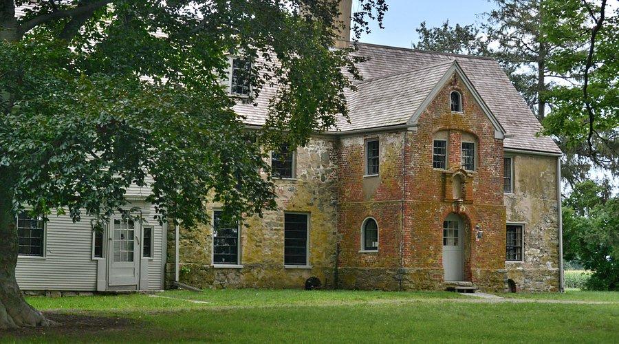 Historic brick and stone house with arched windows, surrounded by trees and grass.
