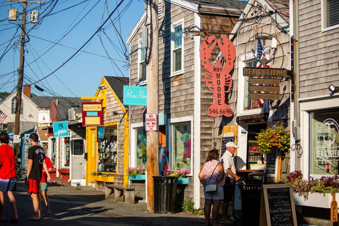 Colorful street with shops, people, and a large lobster sign. Bright, sunny day.