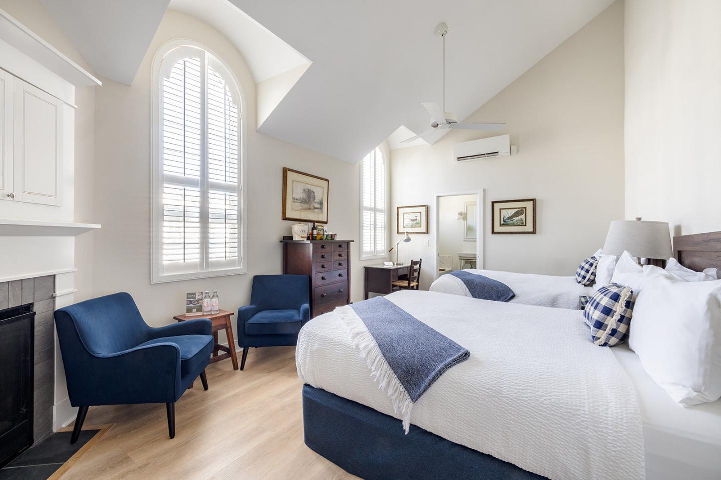 Spacious bedroom with vaulted ceiling, white walls, blue chairs, and large arched window.