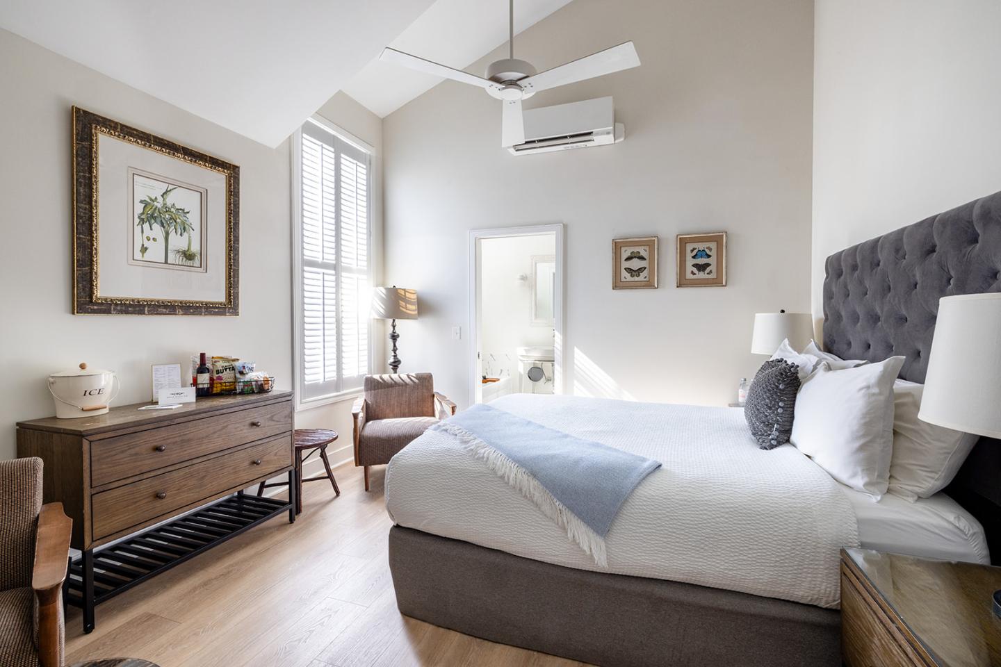 Stylish bedroom with large bed, dresser, and armchair in bright natural light.