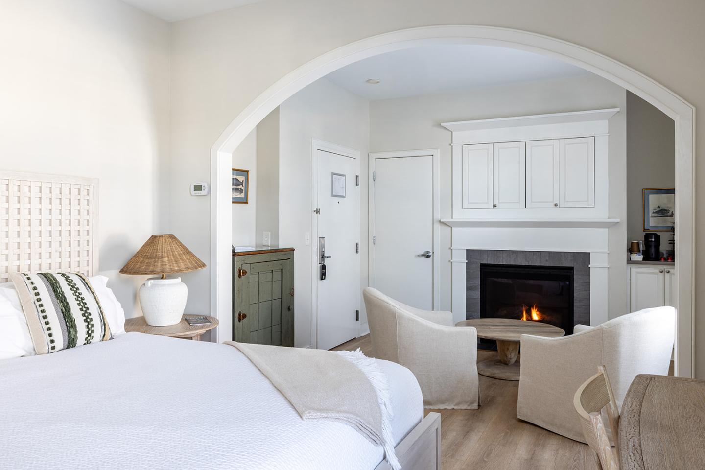 Cozy bedroom with fireplace, white decor, and two armchairs.