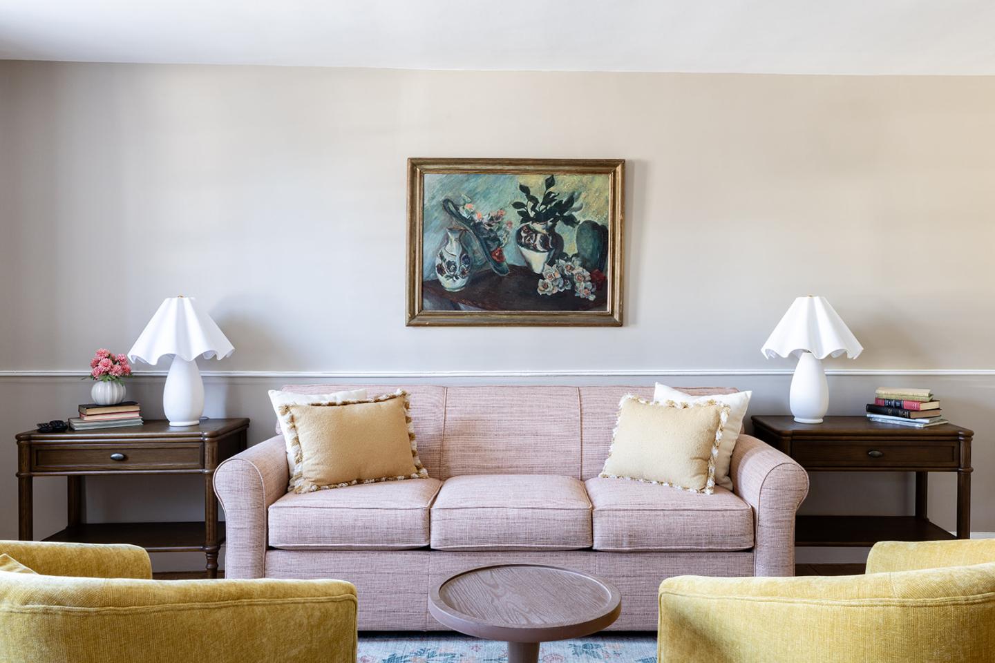 Living room with a pink sofa, yellow pillows, two lamps, and a painting on the wall.