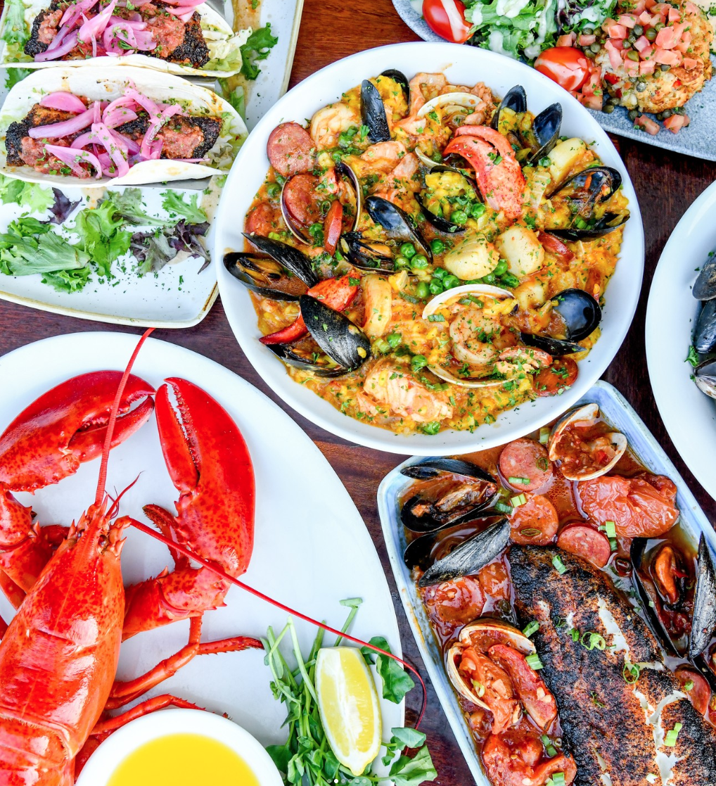 Seafood dishes with lobster, mussels, and tacos on a table.