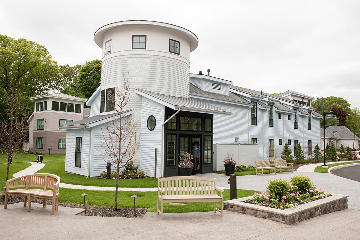 Modern building with round tower, light blue exterior, surrounded by greenery and benches.