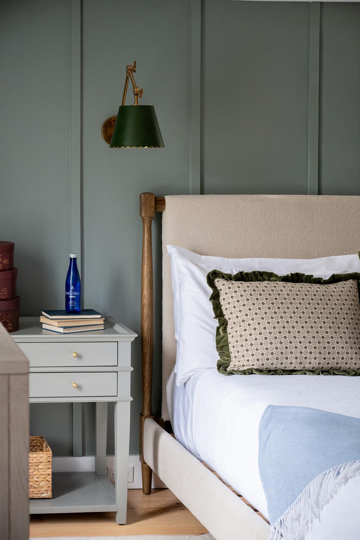 Bed with cushion, green wall light, and gray nightstand.