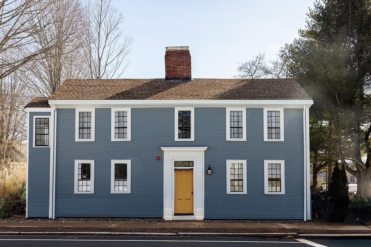 Blue colonial house with a yellow door and symmetrical windows.