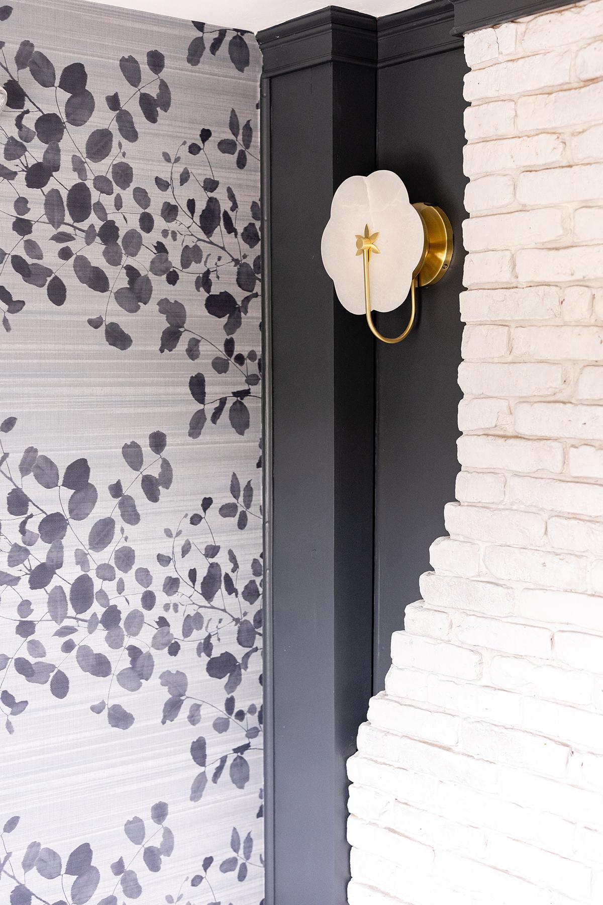 White flower-shaped wall sconce on a patterned wallpaper and brick wall corner.