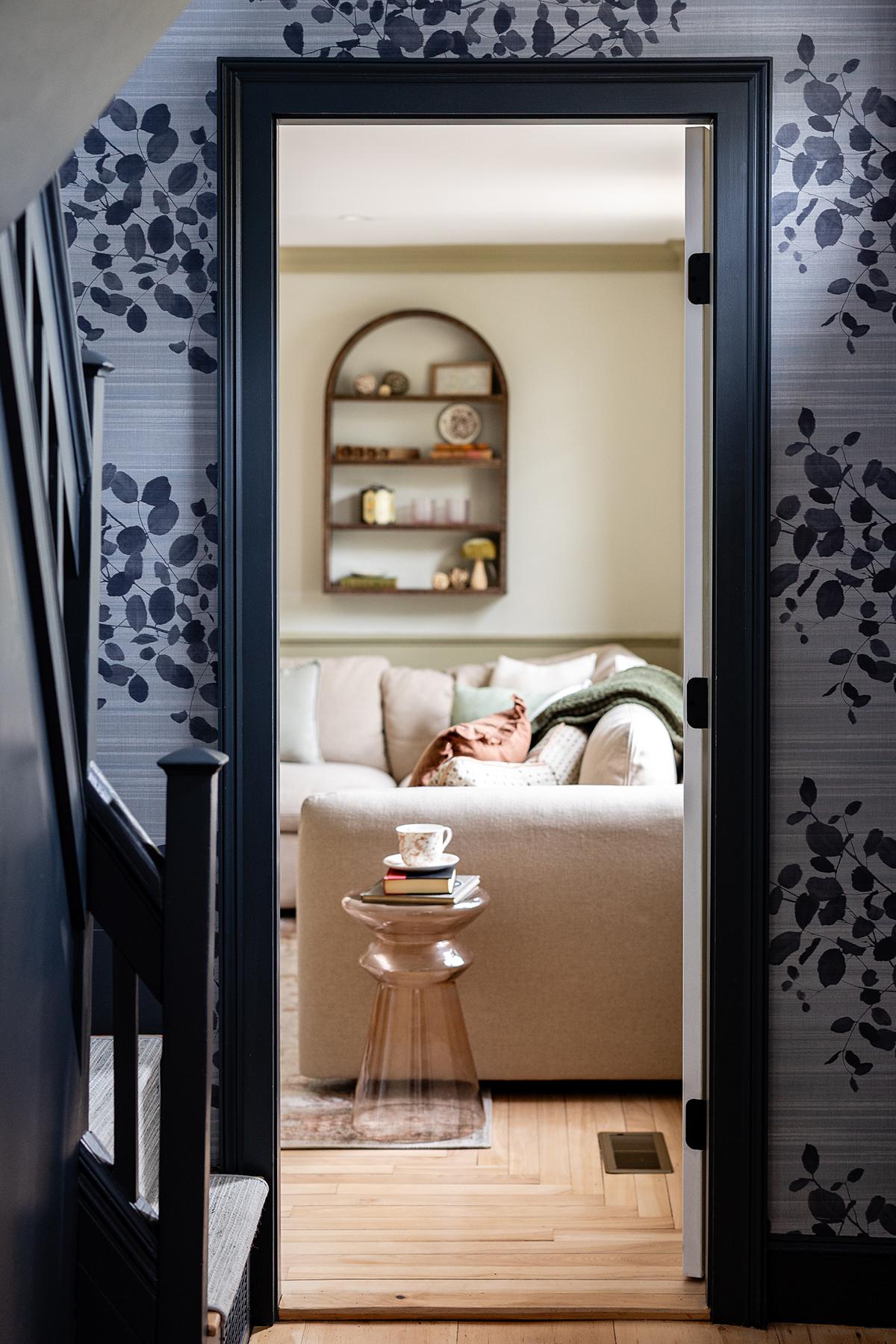Hallway view into a cozy, well-lit room with a couch and wall shelves.