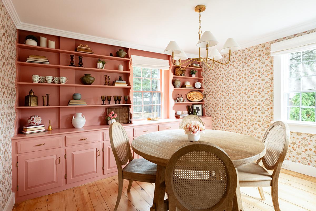 Dining room with pink shelves, floral wallpaper, round table, and window.