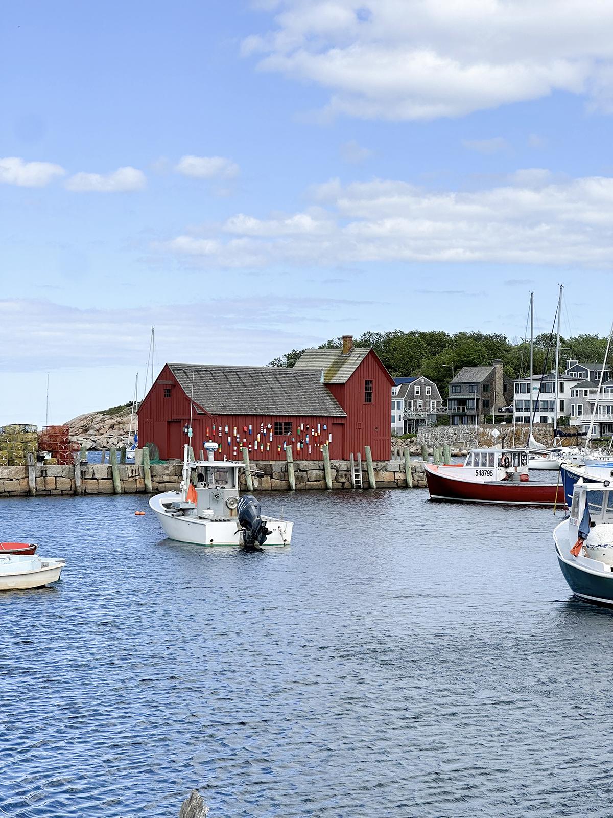 Boats in a harbor near a red building, under a blue sky.